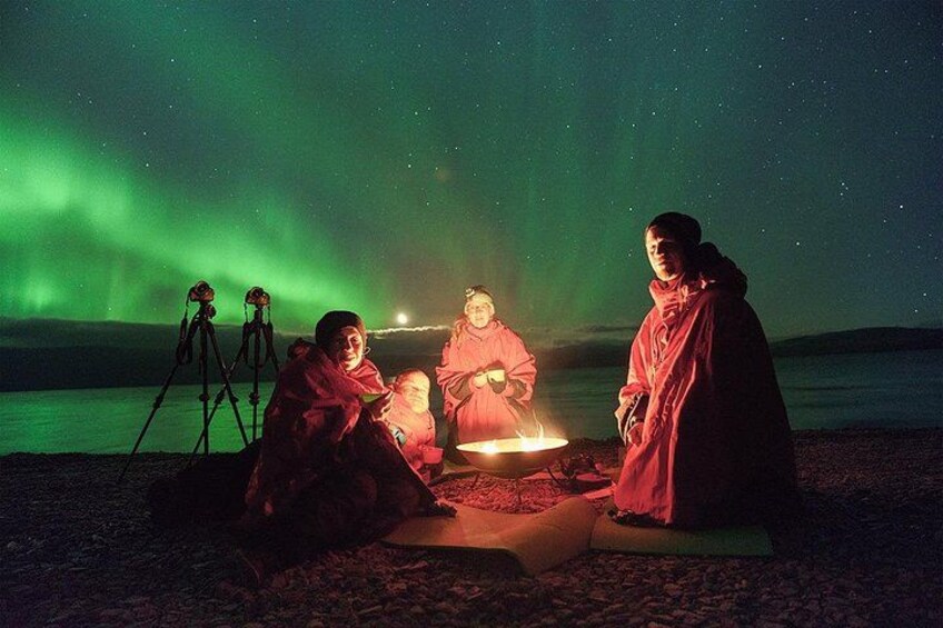 A group of people sitting around a campfire at night with the aurora borealis in the background. 4