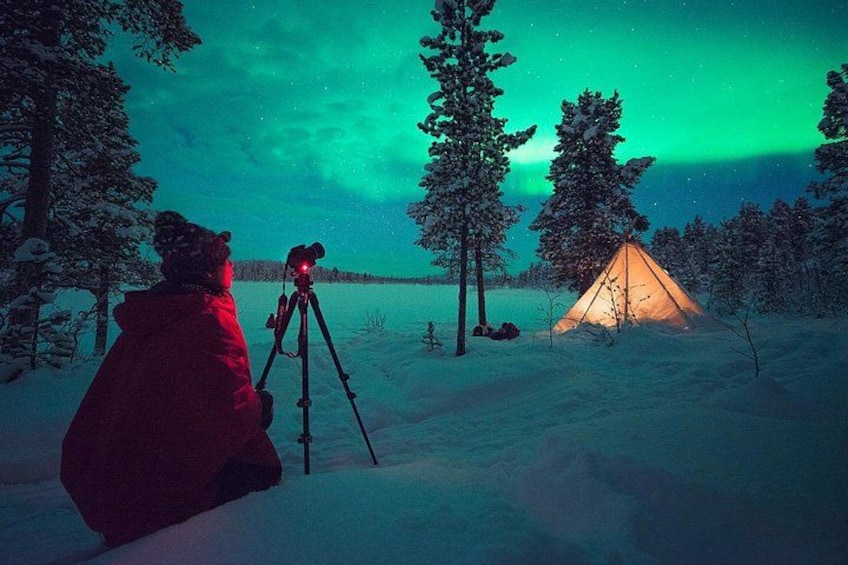 A person with a camera on a tripod, a tent, and a snowy landscape with trees. 1