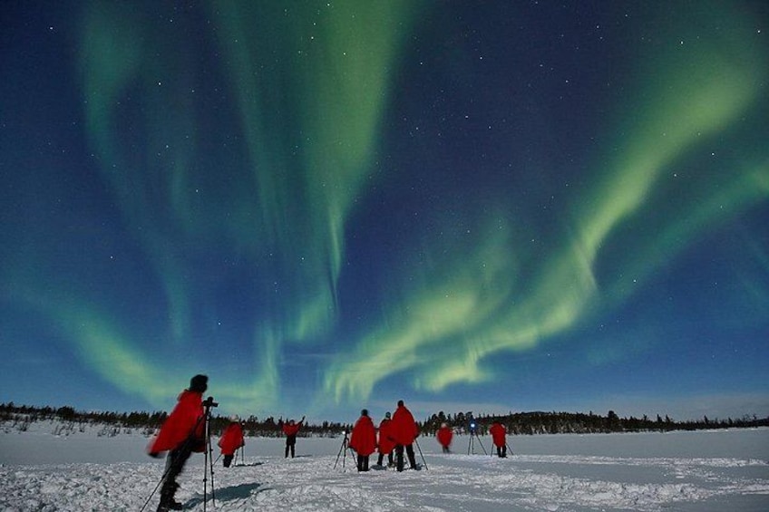 A snowy landscape with people in red jackets observing the Northern Lights. 2