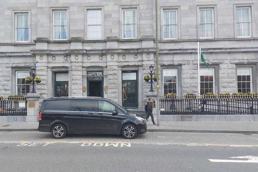 A black van parked on the street in front of a stone building with a flag. 2
