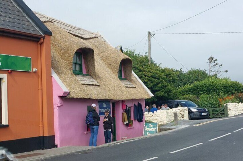 A pink building with a thatched roof, a sign reading "The Sweeney's," and a parked car. 2