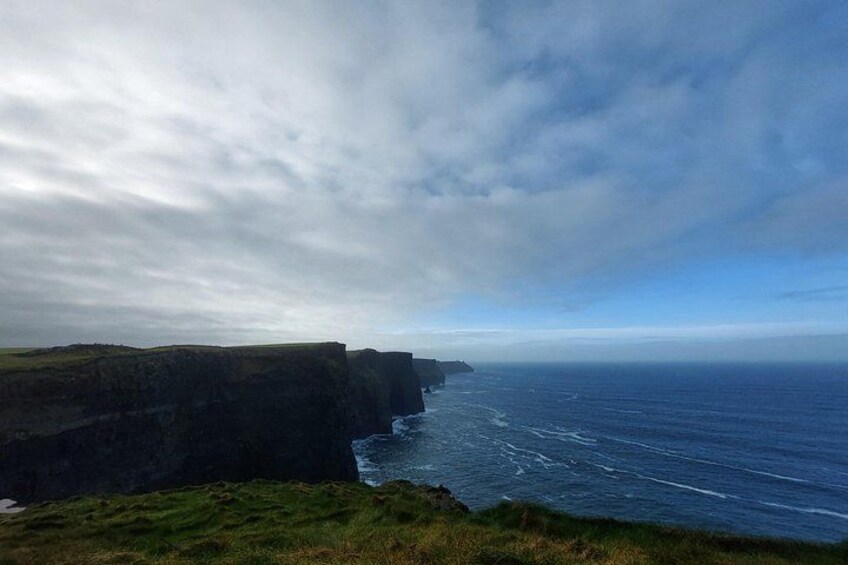 A coastal cliff, ocean waves, and a cloudy sky. 1