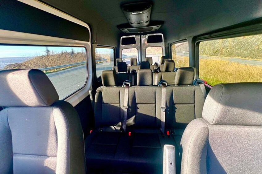 A vehicle interior with multiple rows of seats, a steering wheel, and a dashboard. 2