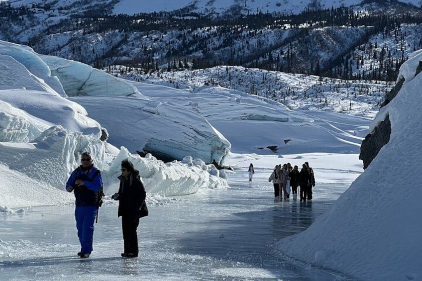 A frozen river with people walking and standing, surrounded by snow-covered mountains and ice formations. 5