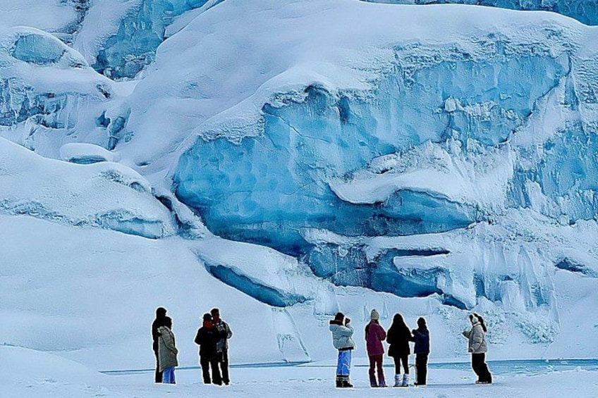 Eine Gruppe von Personen steht auf verschneitem Boden, im Hintergrund ein großer Gletscher. 2