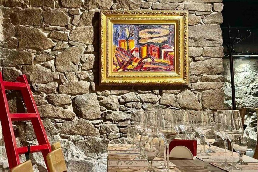 A stone wall with a colorful painting, a red ladder, and scattered wine glasses. 1