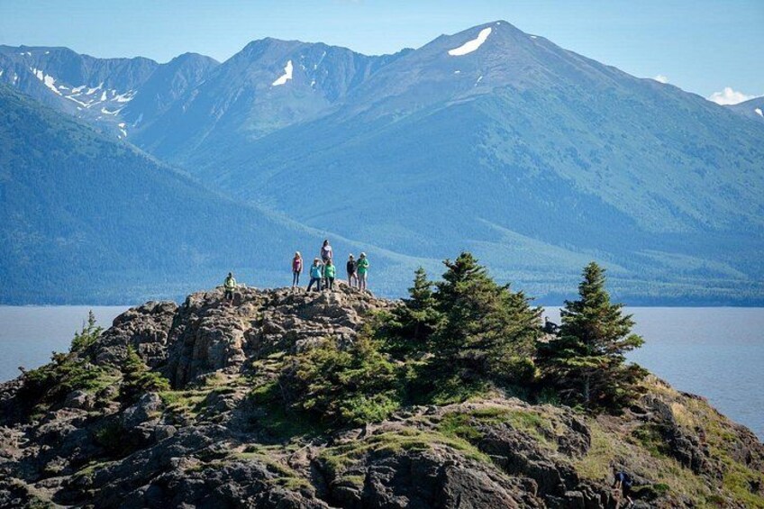 A group of people standing on a rocky outcrop with a lake and mountains in the background. 2