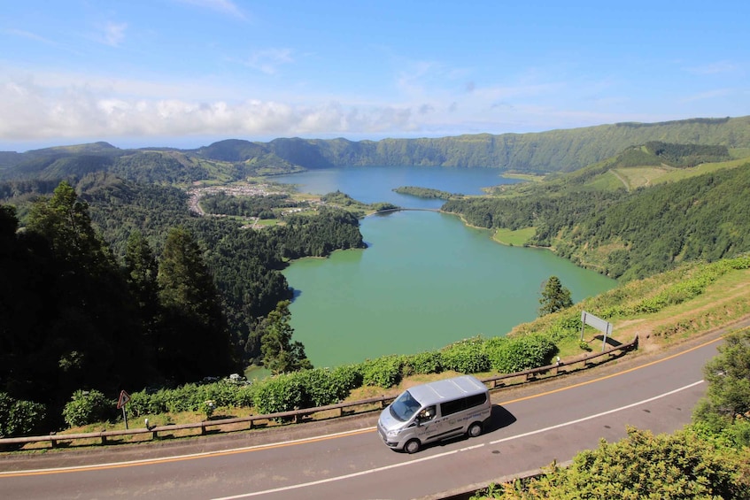 Un furgone argentato percorre una strada con un lago e montagne sullo sfondo. 5