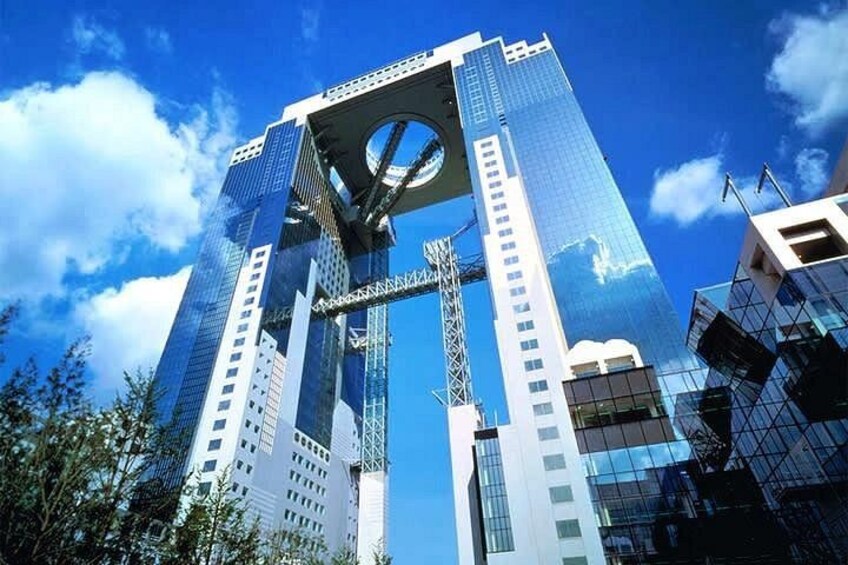 Een modern wolkenkrabber met een opvallend rond element bovenaan, omringd door andere hoogbouw. 1
