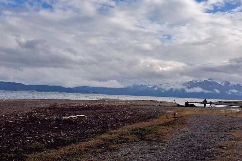 Kystlandskab med en stenstrand, et vandareal og fjerne bjerge under en skyet himmel. 5