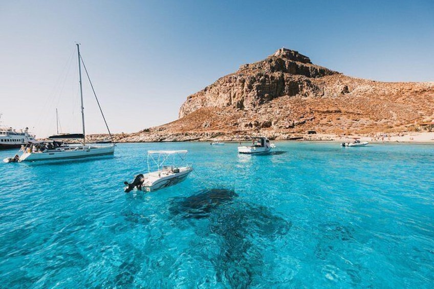Mare cristallino con imbarcazioni, una collina rocciosa e una spiaggia. 2