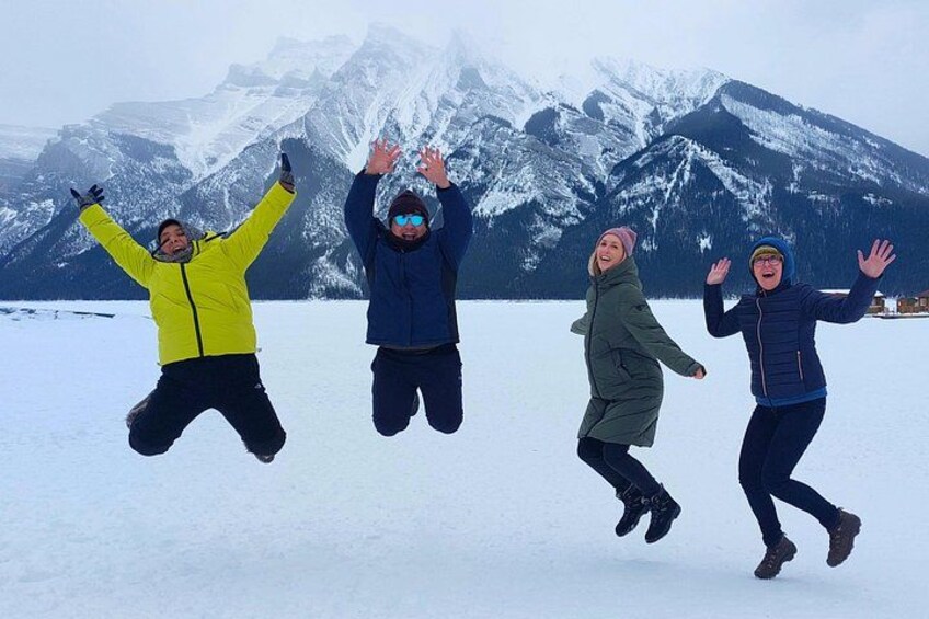Four people jumping in the air with snow-covered mountains in the background. 2