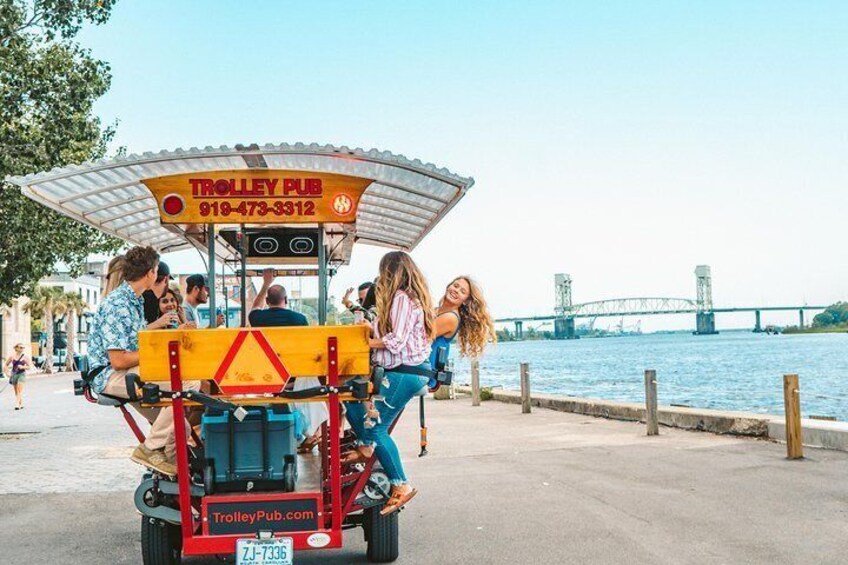 A trolley with people boarding and alighting, a bridge in the background, and a waterfront. 4