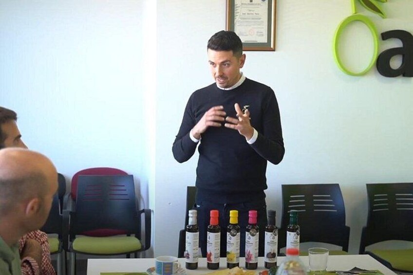 A person standing at a table with bottles and glasses, in a room with chairs and a wall sign. 5