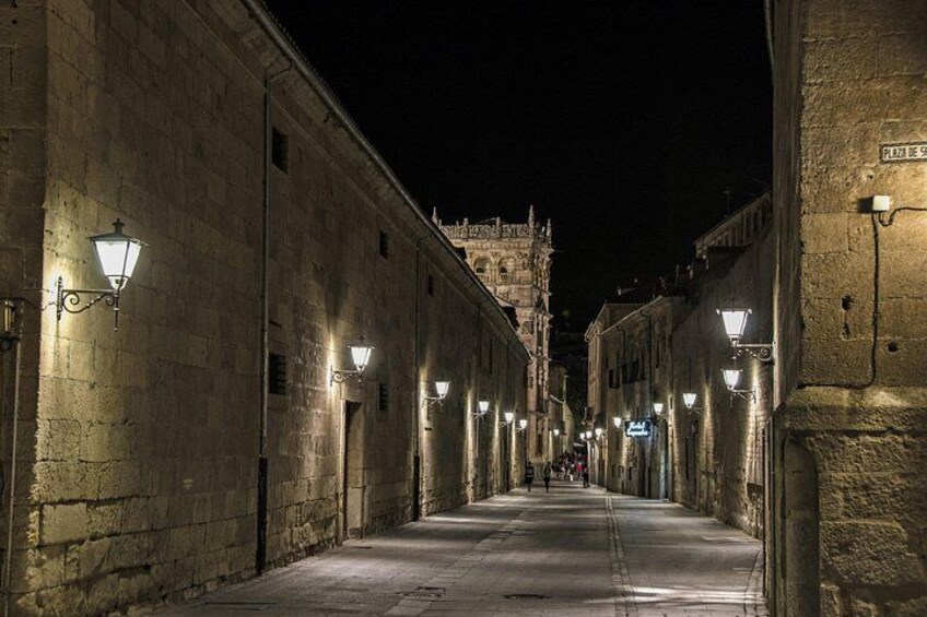 A nighttime street with stone buildings, street lamps, and a distant tower. 4