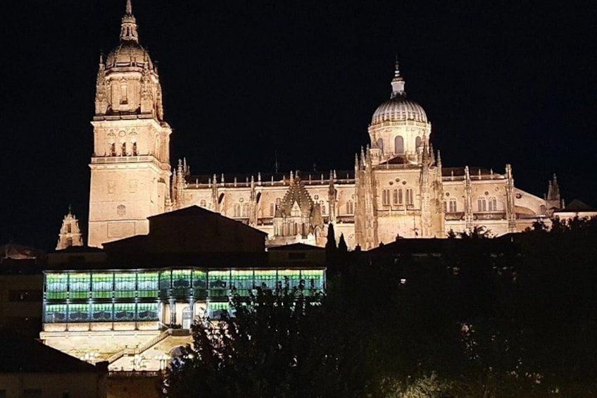 A historic cathedral with a prominent bell tower and a large dome, illuminated at night. 5