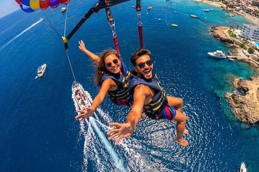 Une personne pratiquant le parachute ascensionnel au-dessus d’une étendue d’eau, avec des bateaux et une côte en arrière-plan. 1