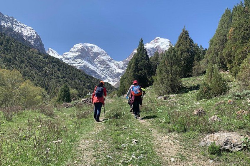 Two hikers on a mountain trail with snow-capped peaks in the background. 3