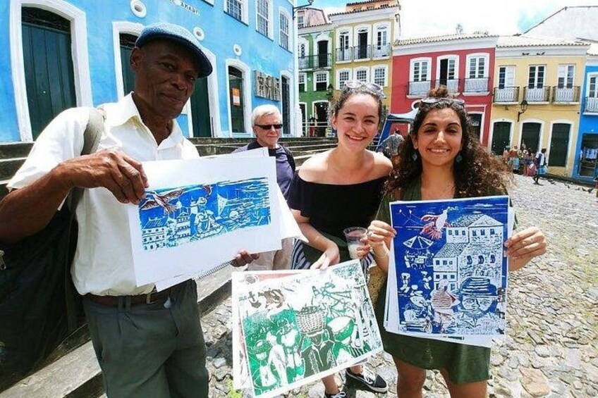 A cobblestone street with colorful buildings, people holding illustrated maps, and a man with a backpack. 1