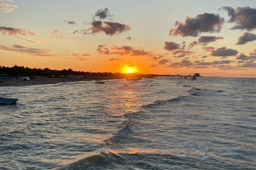 Un coucher de soleil sur une plage, avec des vagues, une jetée et une côte lointaine. 1