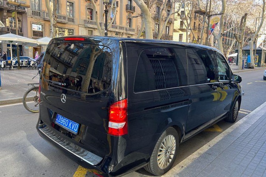 A black van parked on a city street with buildings and trees in the background. 3