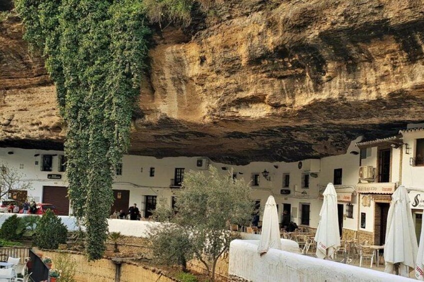 A cliffside building with ivy, outdoor seating, and a rocky landscape. 2