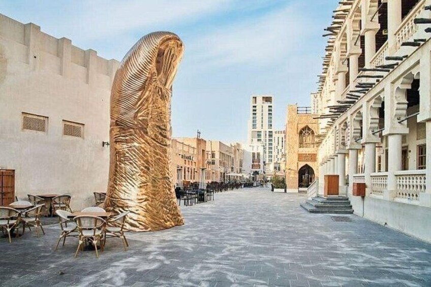 Una calle con una gran escultura dorada, edificios y mesas al aire libre. 4