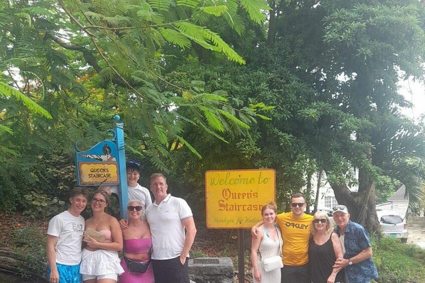 Un grupo de personas de pie frente a un letrero que dice 'Welcome to Queen's Staircase'. 1