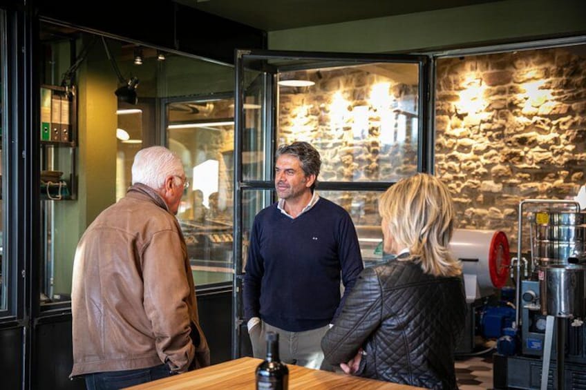 Tres personas de pie frente a una barra en una cafetería, con una pared de piedra y cafeteras al fondo. 1
