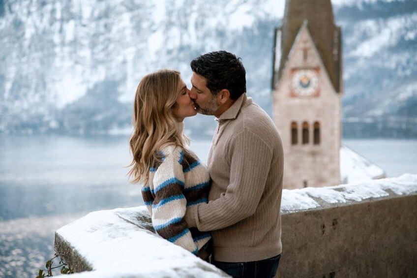 Una pareja se abraza en un saliente nevado con una torre del reloj al fondo. 3
