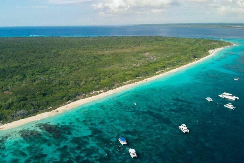 A coastal landscape with a sandy beach, clear turquoise waters, and several boats. 4