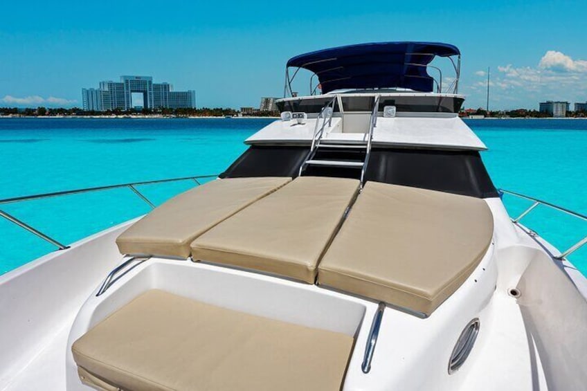 A boat with a blue canopy and beige cushions on the deck, with a clear blue sea and buildings in the background. 5