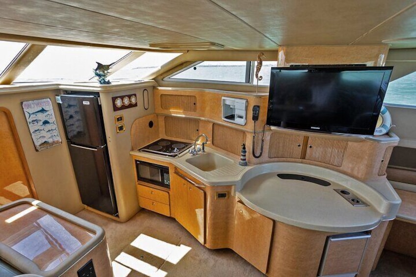 A compact kitchen with a refrigerator, microwave, stove, sink, and a television. 3