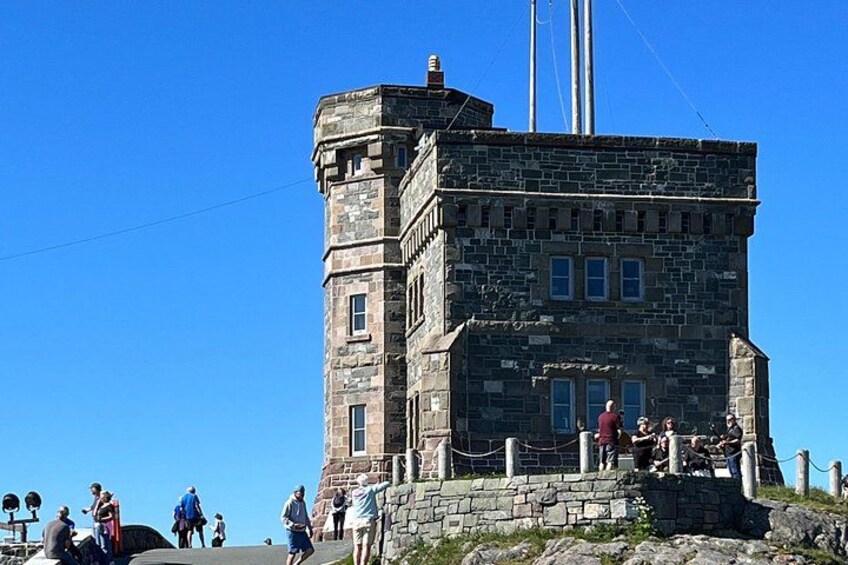 A stone tower with a flagpole, surrounded by a stone wall and a few people. 2