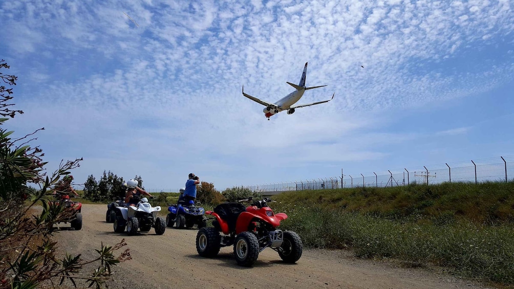 A dirt road with ATVs and a person in a blue shirt. An airplane is flying overhead. 3