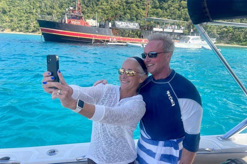 A person taking a selfie on a boat with a large ship in the background. 3