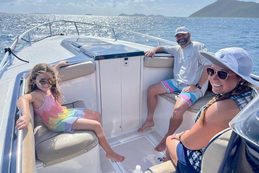 A boat with three people on board, a clear sky, and a body of water with distant land. 2