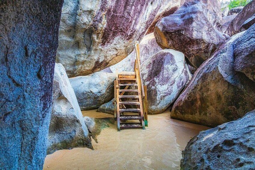 A wooden ladder leading up a rocky path surrounded by large boulders. 1