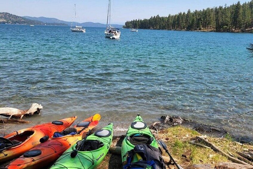 Des kayaks sont alignés sur la rive d’un lac, avec des voiliers en arrière-plan. 4