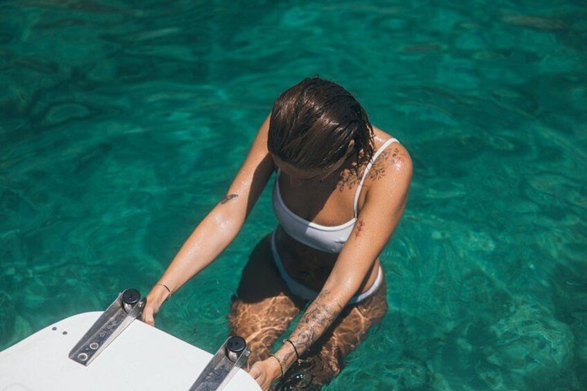 A person in a swimsuit holding a white surfboard in clear blue water. 2