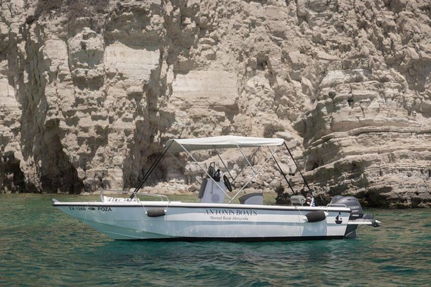 A white boat named 'Antonius Boats' with a canopy, anchored near rocky cliffs. 3
