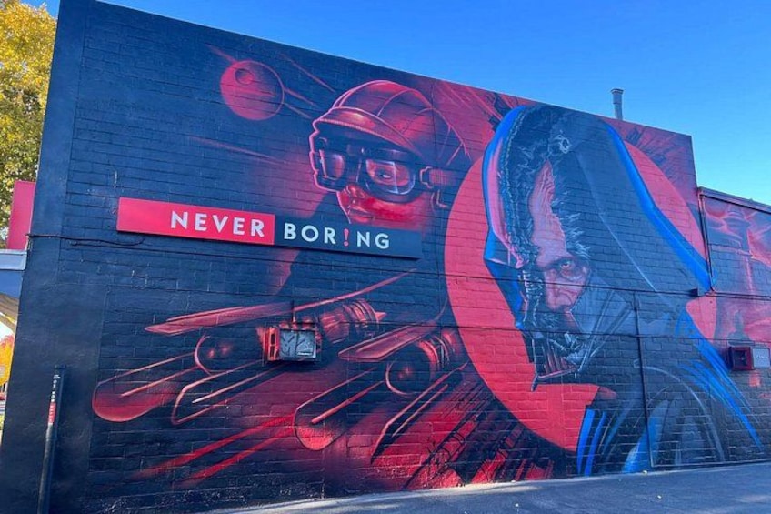 Ein Wandgemälde mit Weltraumthema, das einen Helm, eine Rakete und die Aufschrift 'NEVER BORING' zeigt. 1