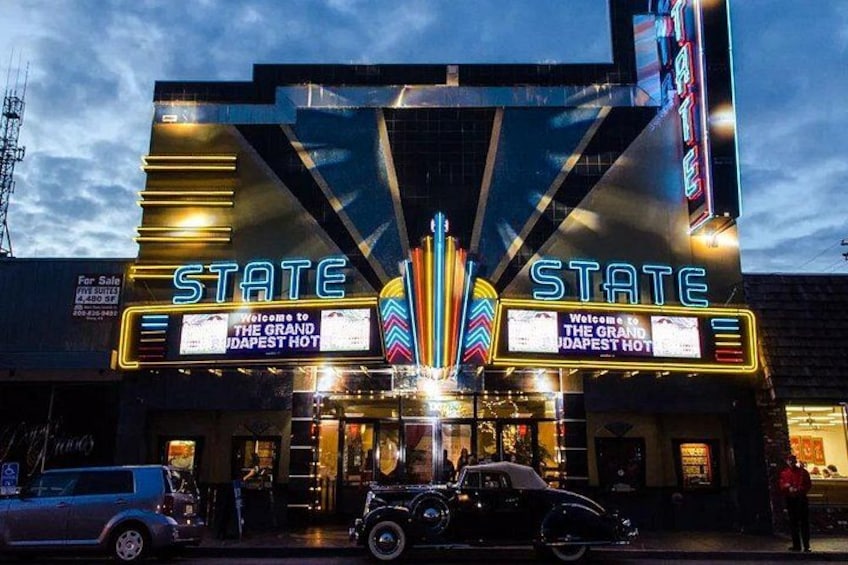 Ein Kino im Vintage-Stil mit Neonreklame und einem Oldtimer davor. 2