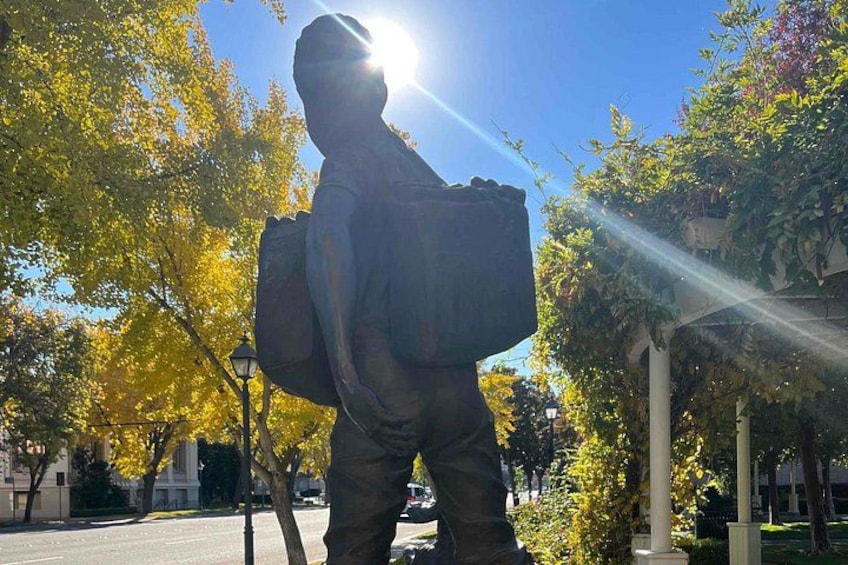 Eine Statue einer Person mit Rucksack, Bäume mit gelben Blättern und ein klarer Himmel. 5