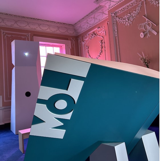 Eine moderne Skulptur mit geometrischen Formen und den Buchstaben 'MOL' in Weiß vor einem türkisfarbenen Hintergrund. 3