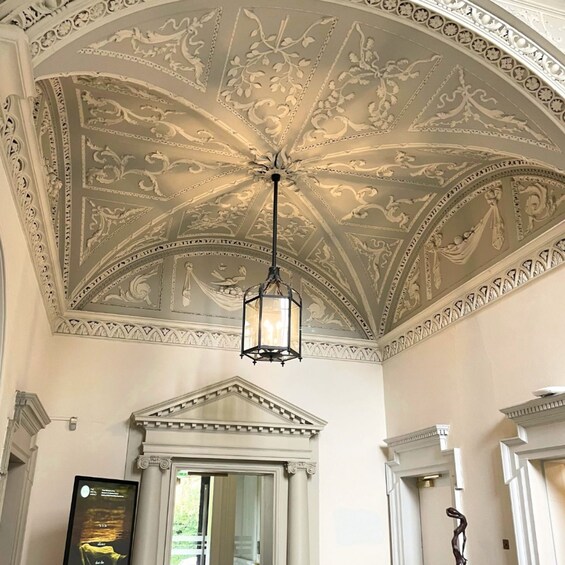 Ein prachtvoller Innenraum mit einer detailreichen Decke, einem hängenden Laternenleuchter und klassizistischen architektonischen Elementen. 4