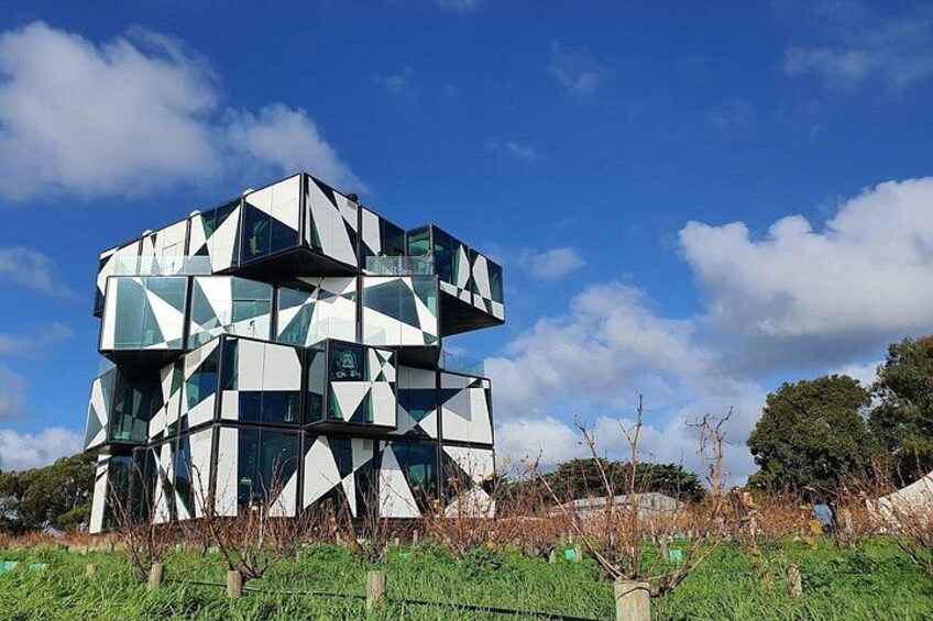 A modern, geometric building with glass panels and a clear blue sky. 1