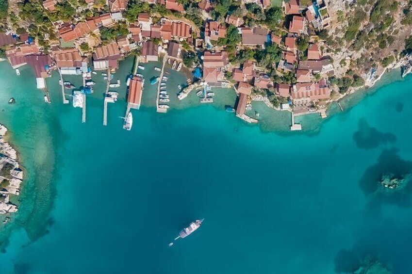 An aerial view of a coastal town with buildings, boats, and clear turquoise waters. 1