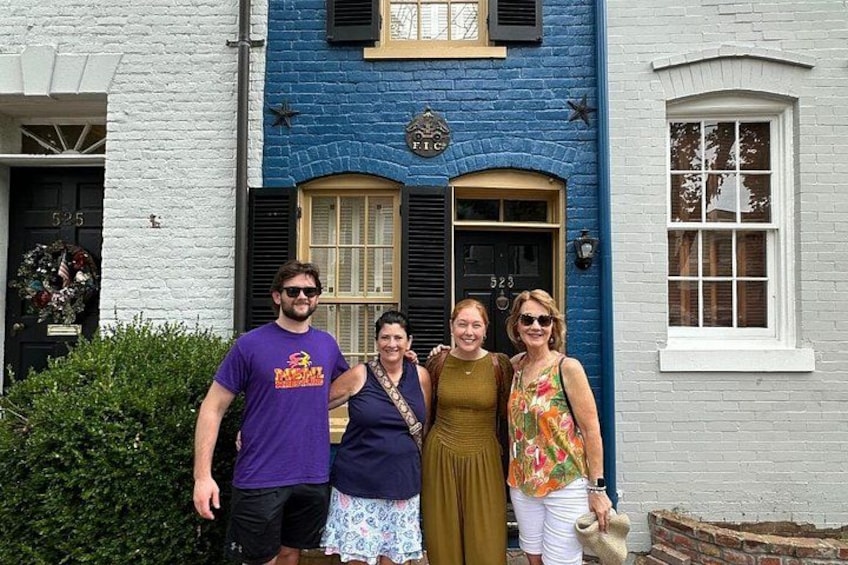 A group of people standing in front of a blue building with a black door and a window. 4