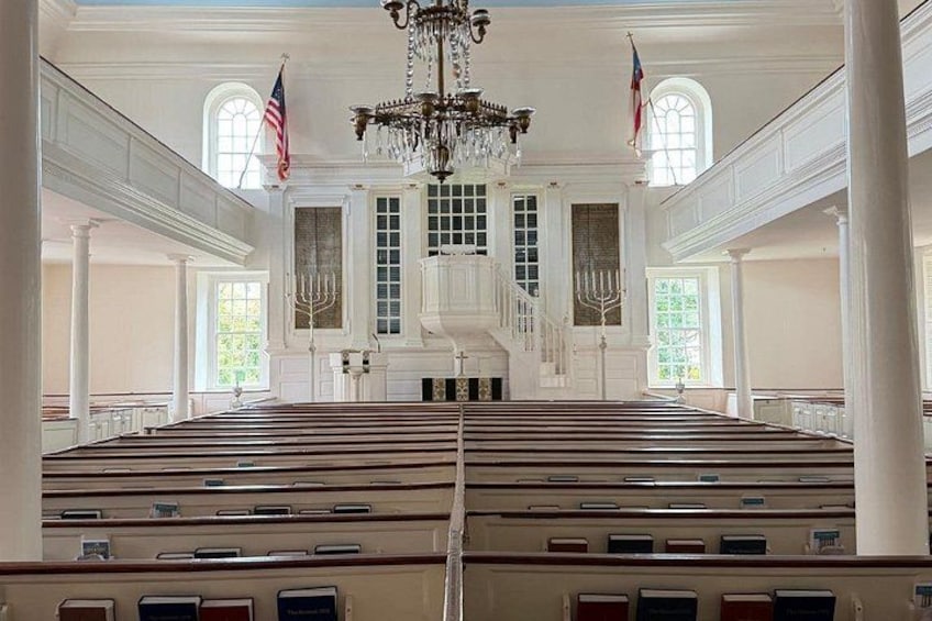 A grand hall with rows of wooden pews, a chandelier, and flags. 5